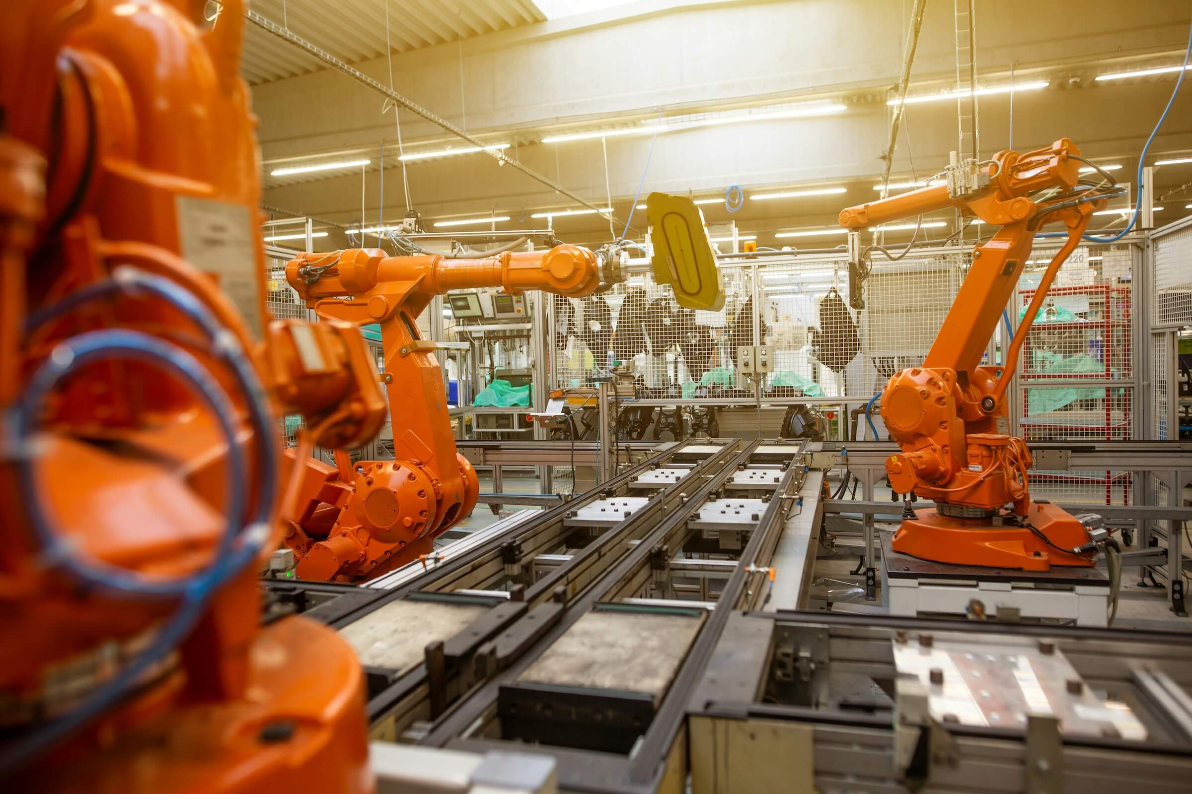 Wnętrze hali fabrycznej z kilkoma pomarańczowymi robotami przemysłowymi